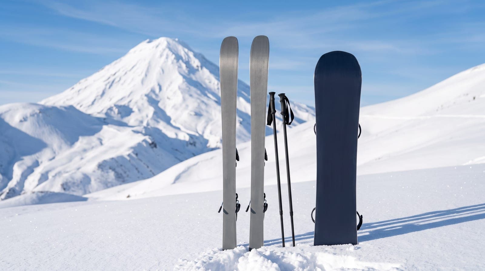 Karda yan yana dikili duran kayak takımı ve snowboard; arka planda karlı volkanik dağ